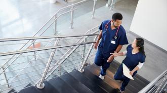 Two health care workers speak to each other while walking up the stairs.